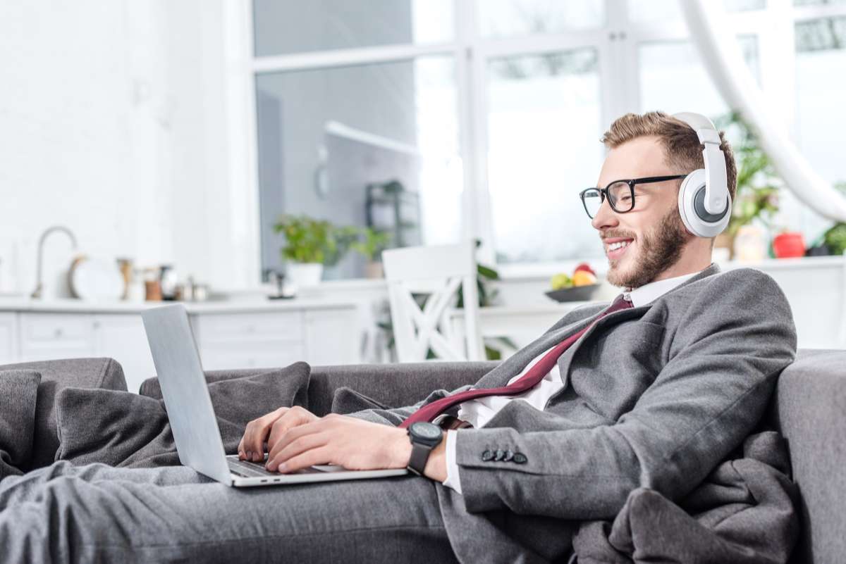 Businessman in glasses wearing headphones and using laptop on couch (R) (S)