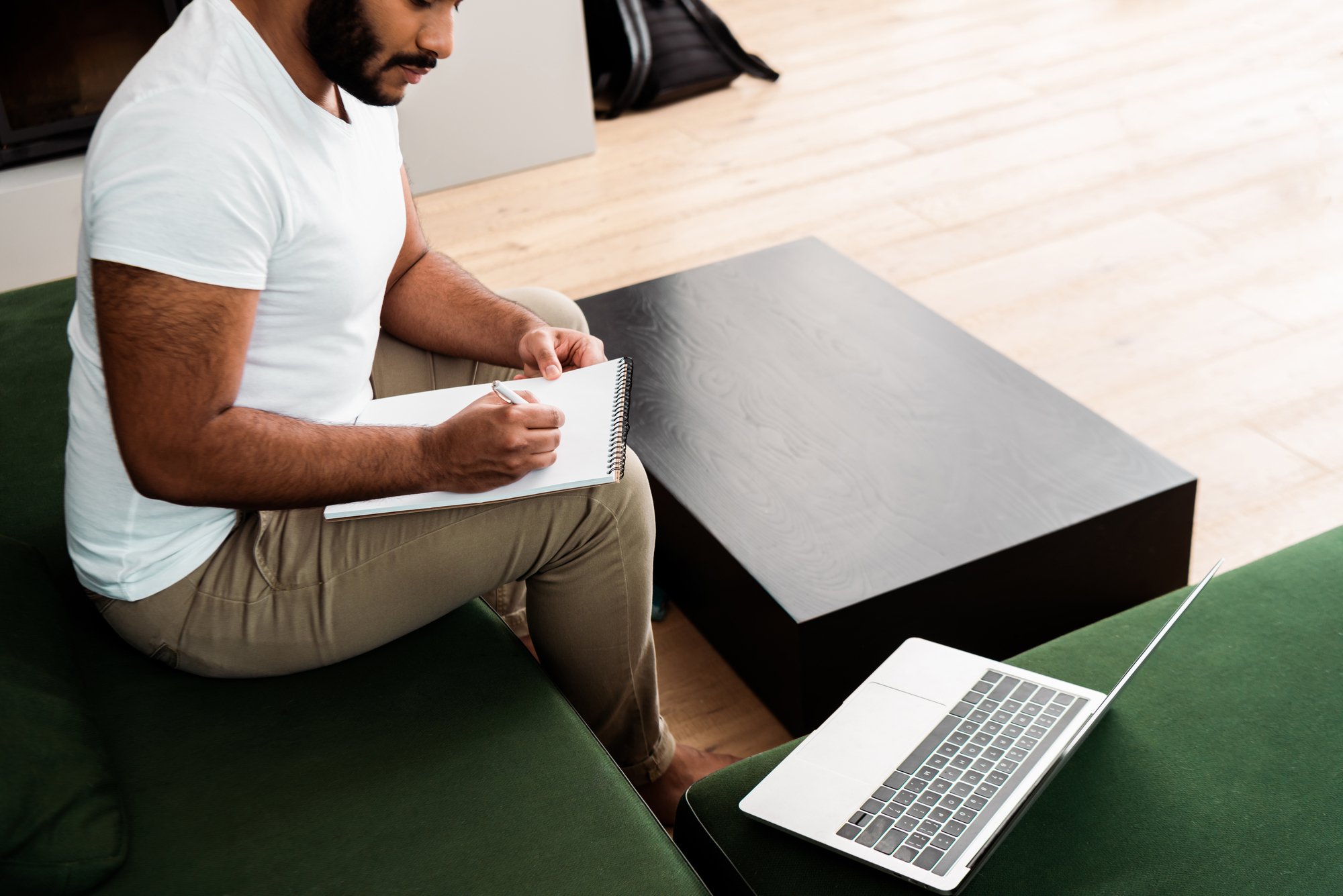 Cropped view of bearded african american man writing in notebook near laptop, study online
