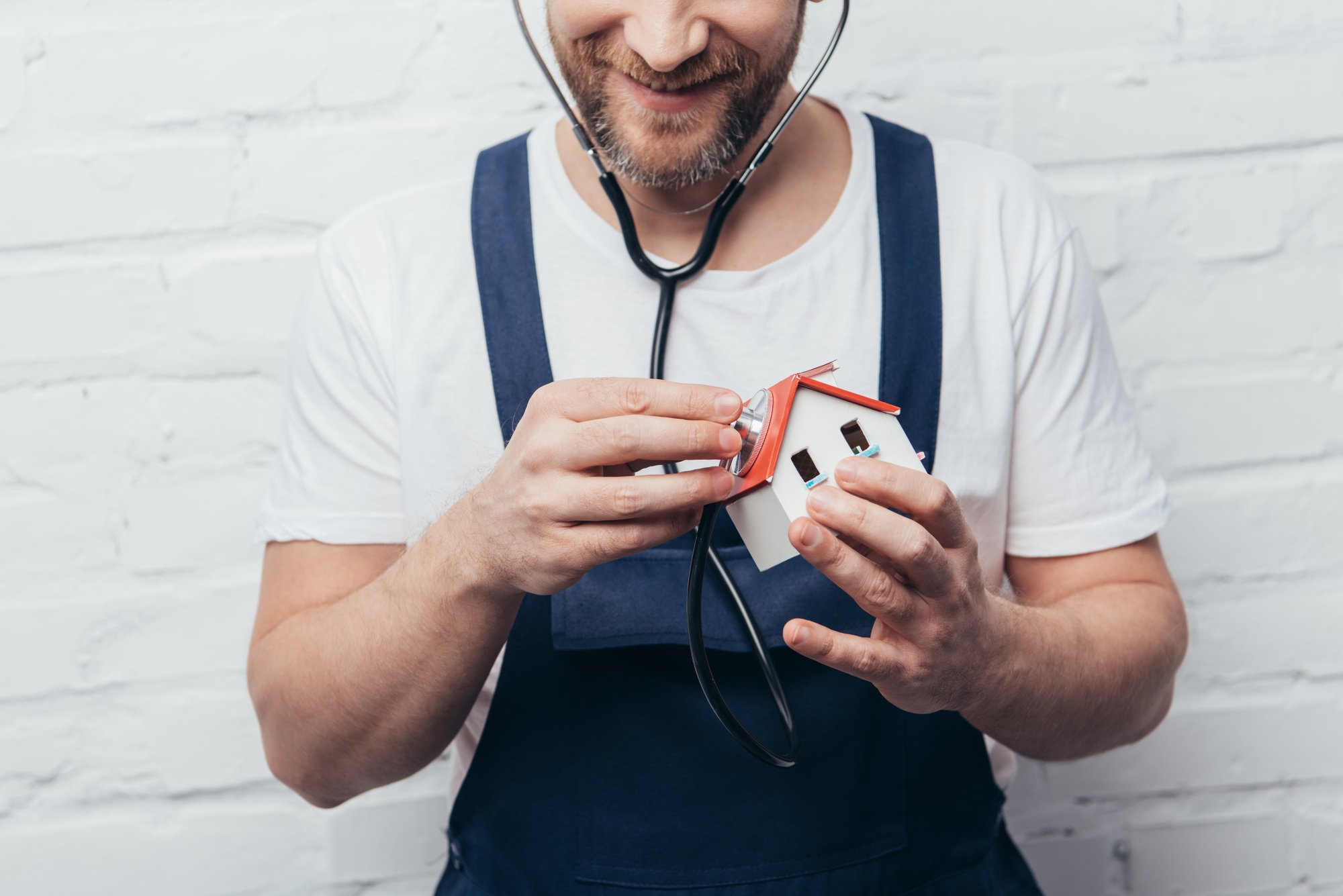 Partial view of male handyman checking house figure by stethoscope, home inspection concept