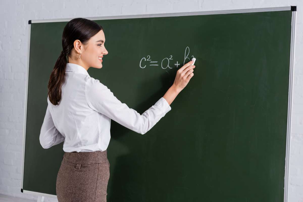 Smiling teacher writing mathematic equation on chalkboard (S) (R)