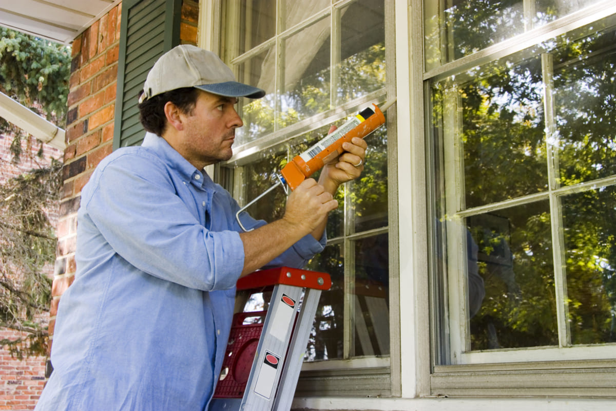 A man caulking windows outside a home, property management vs self management concept