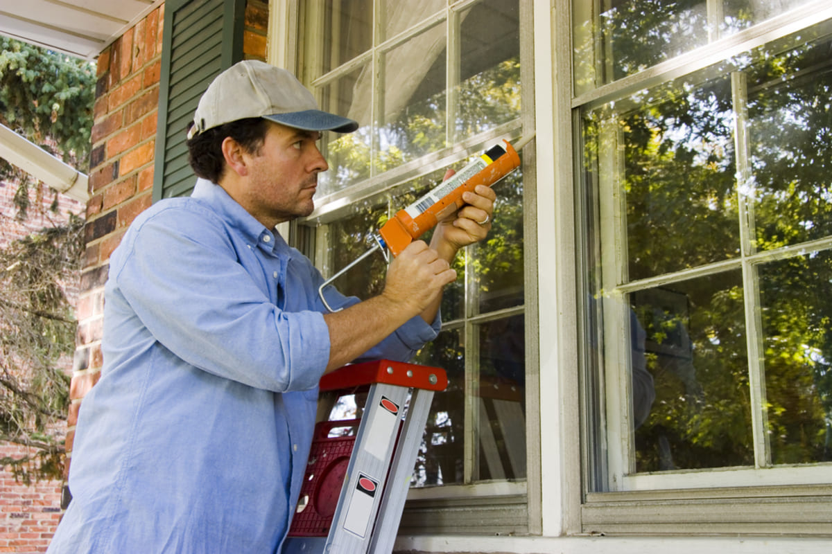A man caulking windows outside a home, property management vs self management concept