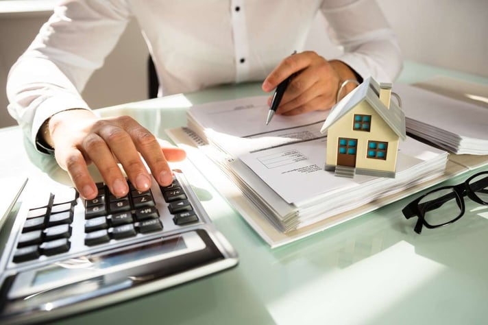 Businessmans hand calculating invoice with house model in office