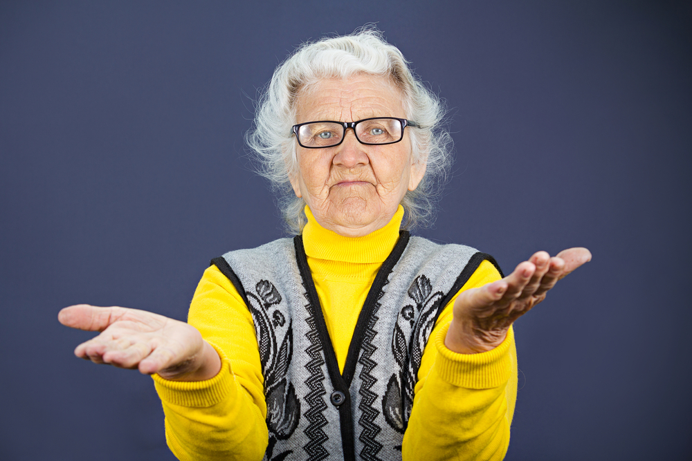 Closeup portrait, clueless senior, mature, elderly woman, arms out asking why whats problem who cares so what I dont know, isolated blue background. Negative human emotion, facial expression feeling