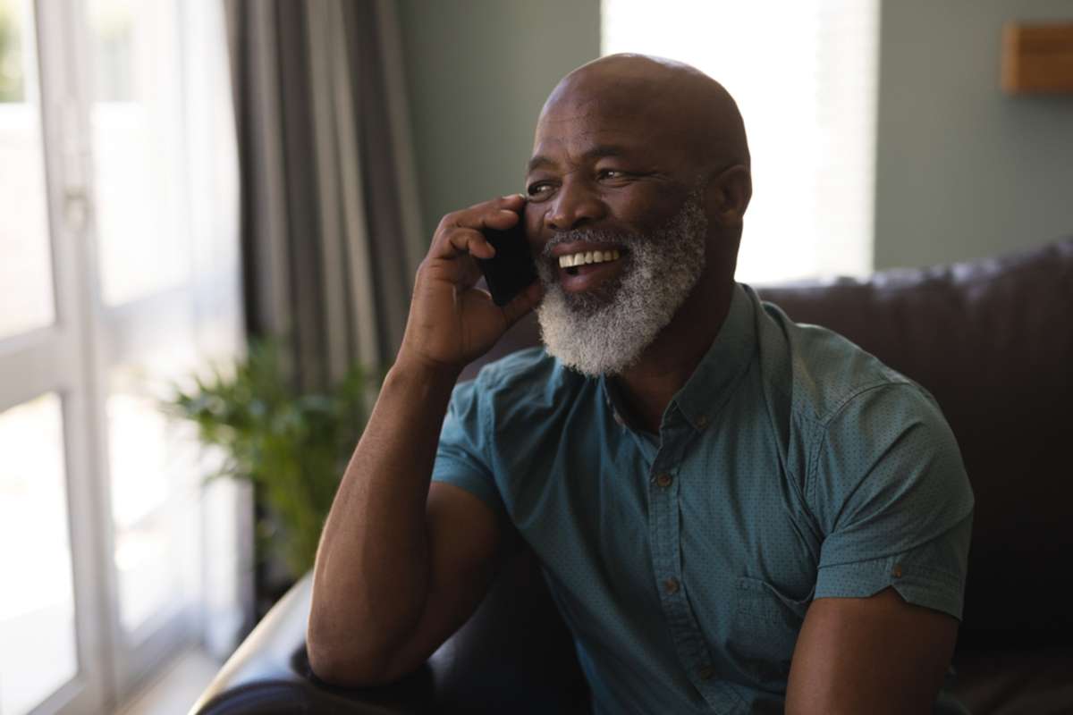 Front view of happy senior man talking on mobile phone in living room at home