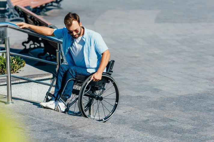 Handsome man in sunglasses using wheelchair on stairs without ramp