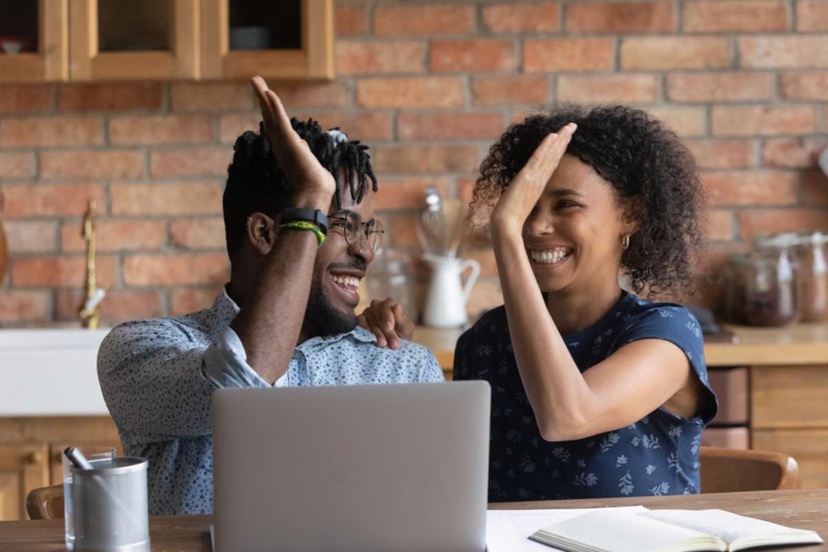 Happy excited Black mixed race couple celebrating financial success at laptop