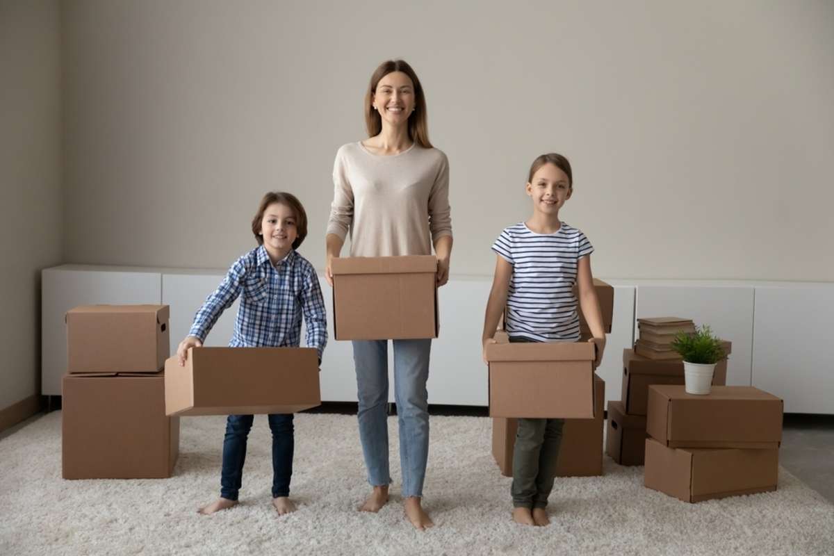 Happy family young mother and joyful little children son daughter holding carton boxes with belongings posing together in new renovated living room