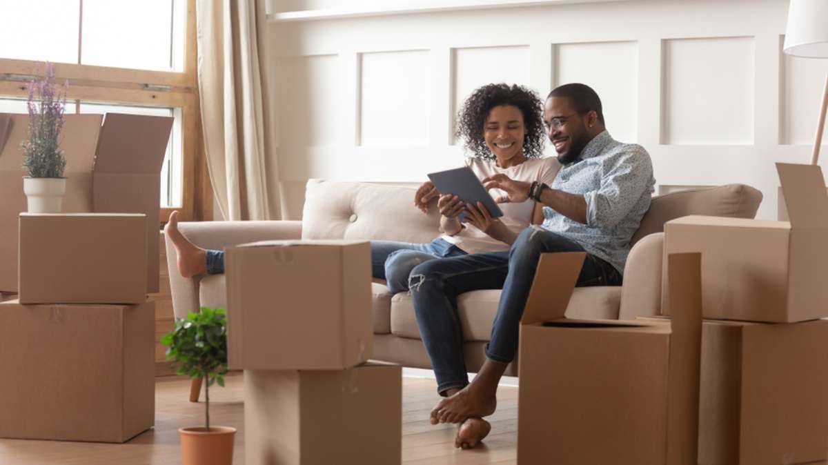 Happy young african couple use digital tablet discuss interior design renovation ideas sit on sofa