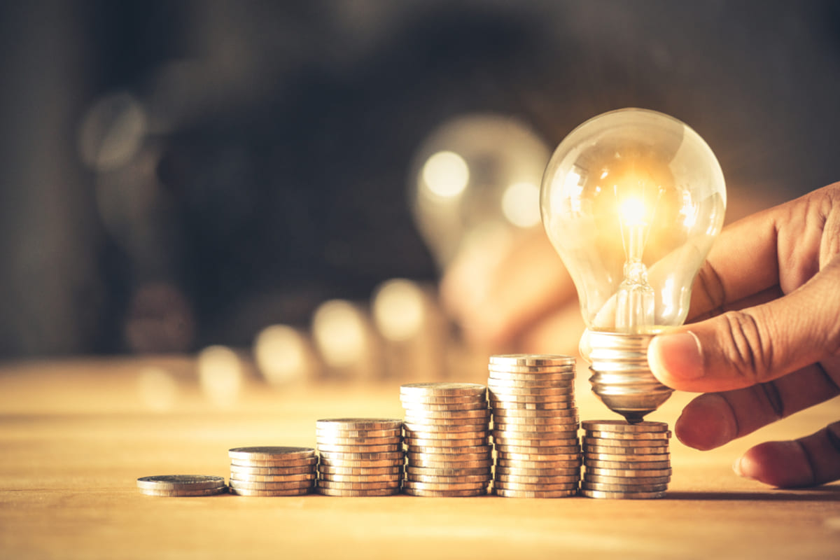 Lit-up lightbulb on a stack of coins, smart investment concept