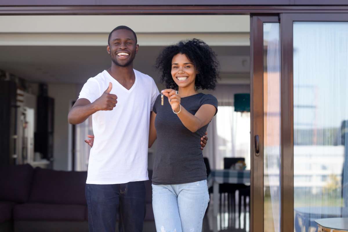 Overjoyed african married couple standing on summer terrace porch near new modern house
