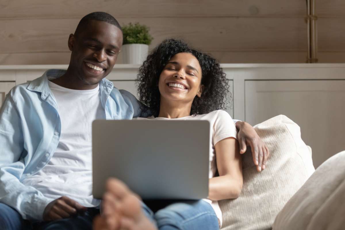 Overjoyed biracial young couple have fun laugh watching funny video on computer relaxing on couch together