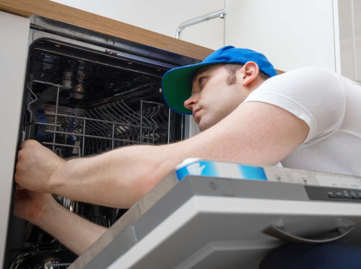 Professional handyman fixes a dishwasher, is buying a home warranty worth it concept