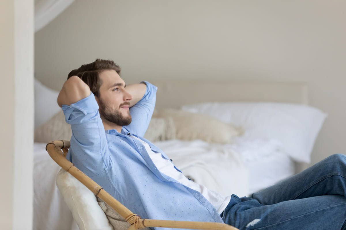 Side view relaxed young man sitting on cozy armchair with folded arms behind head