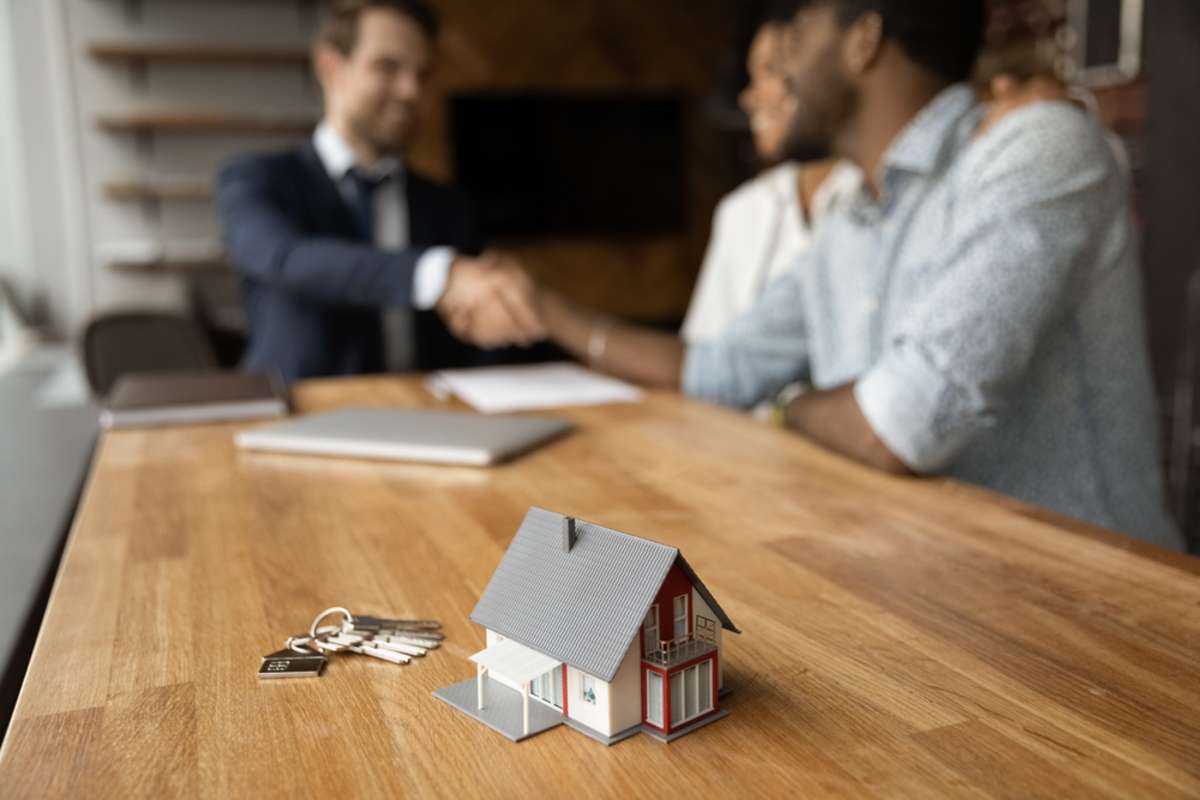 Smiling young man broker realtor real estate agent shake hands of happy black couple clients