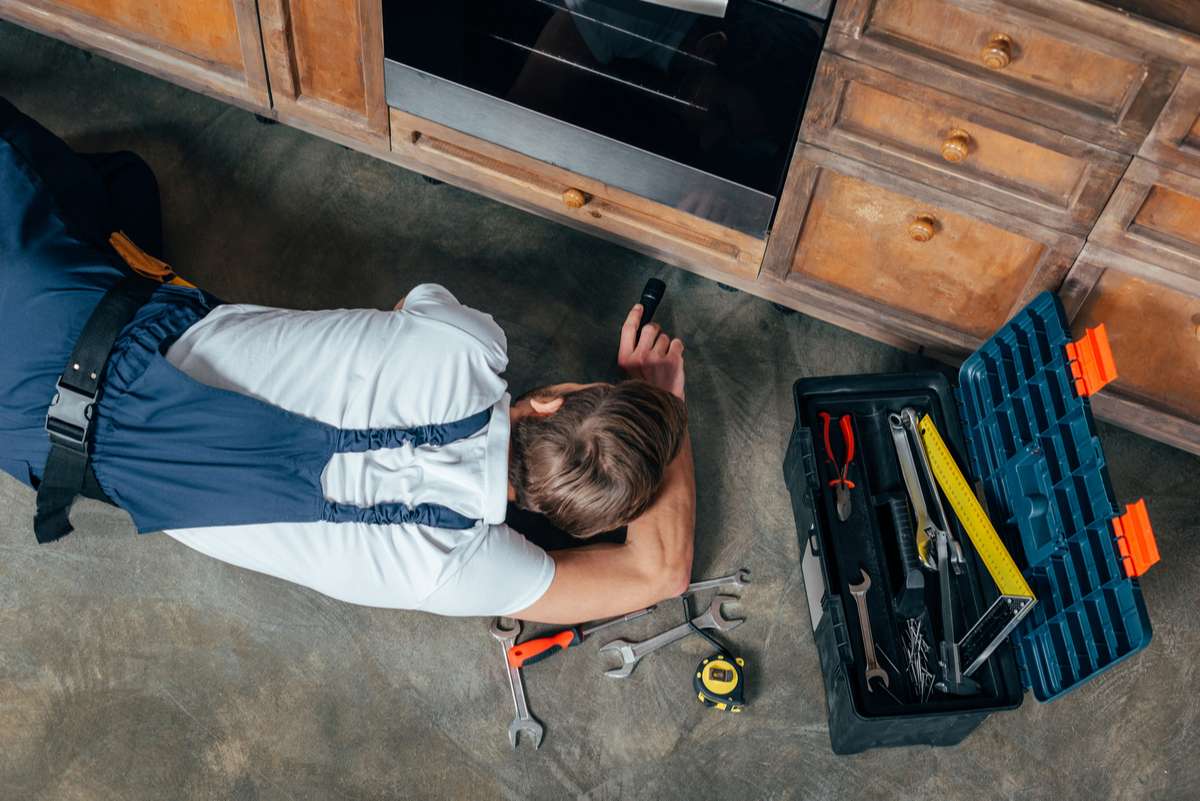 Top view of young repairman checking broken oven with flashlight