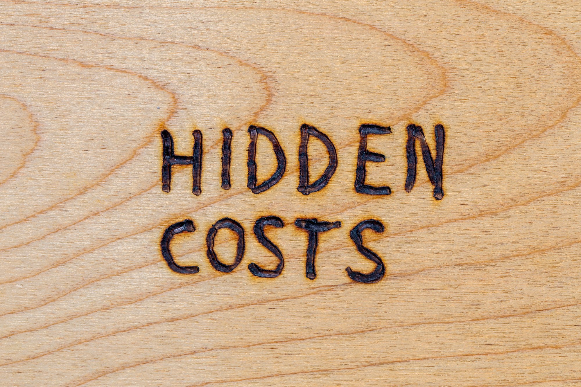 The words hidden costs handwritten with woodburner on flat wood surface - directly above flat lay view