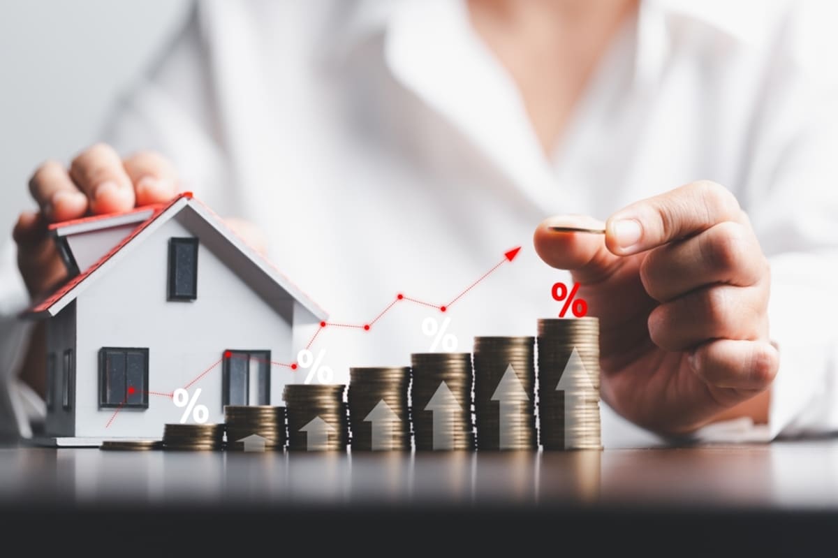 Business woman hand stacks coins by house model and graph representing financial gains