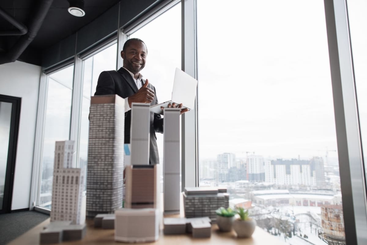 Confident investor man behind buildings models on desk