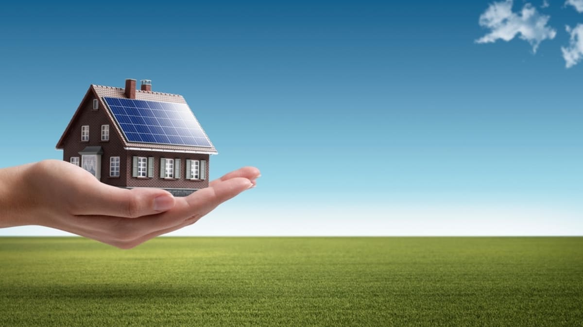 Hand holding an energy-efficient model house with solar panels