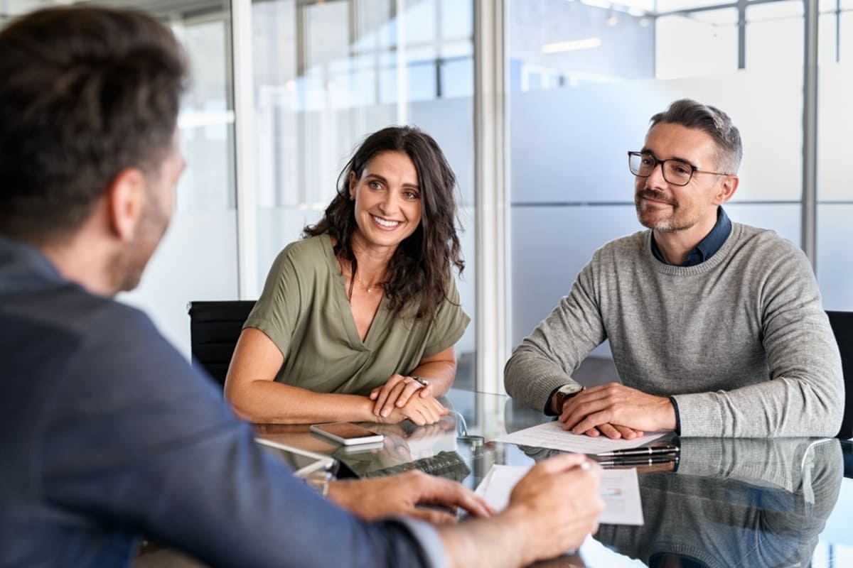 Mid-adult couple listening to property manager during meeting in conference room