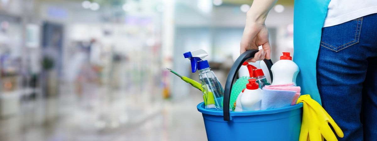 A cleaning woman is standing inside a building holding a blue bucket